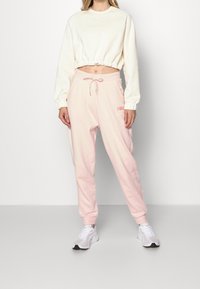 Krämmel färgad kort sweatshirt med elastisk nederkant, kombinerad med ljusrosa joggers med dragsko i midjan och logodetalj. Vita sneakers som accent.