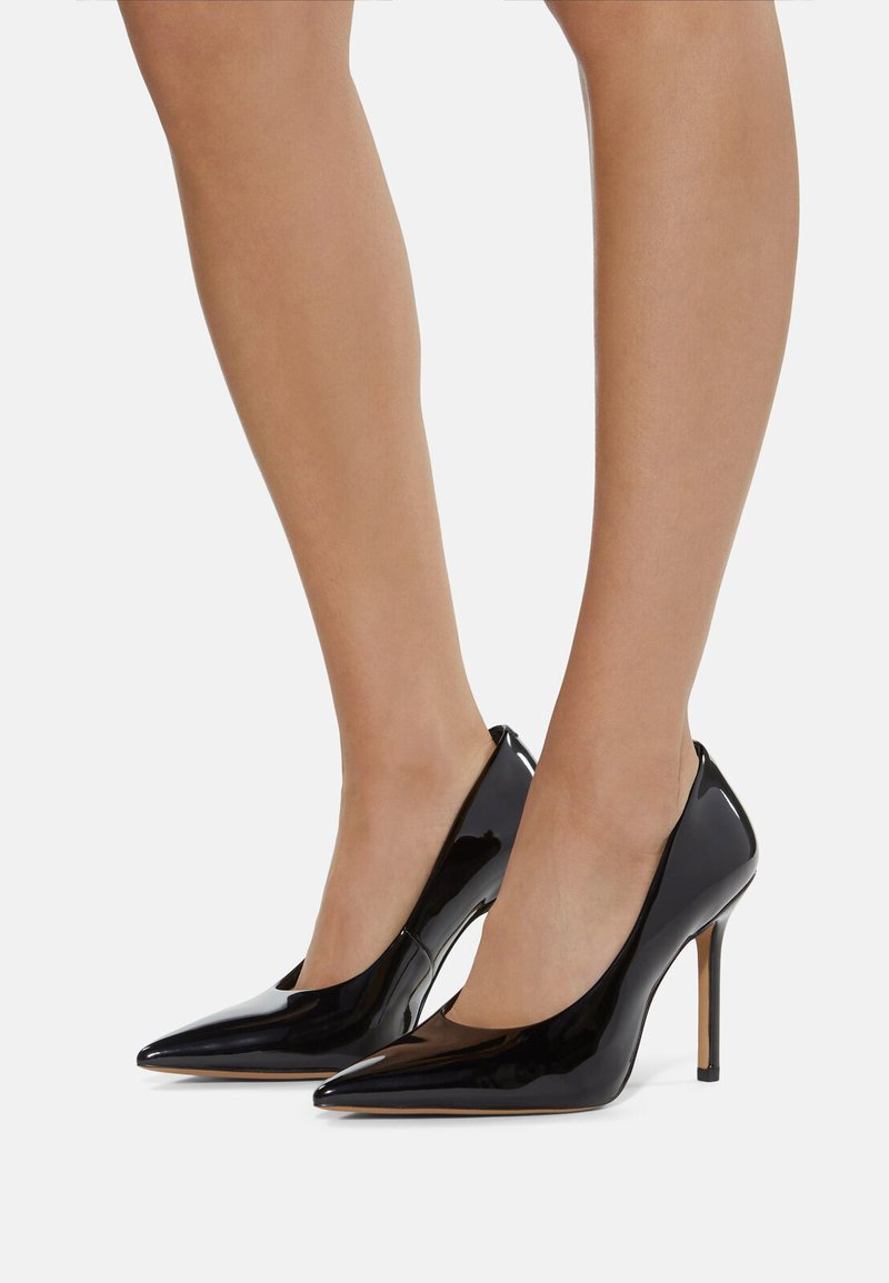 Dei tacchi alti in pelle verniciata nera con design a punta e tacco a stiletto, caratterizzati da un taglio basso lungo i lati per un aspetto elegante.