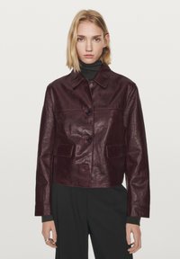 Bordeauxfarvet cropped læderjakke med krave, to forlommer og knaplukning; blank tekstur og struktureret silhuet.