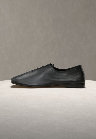 Μαύρο δερμάτινο παπούτσι χωρίς κορδόνια με μυτερή μύτη, διακοσμημένο με μικρές καρφίτσες κατά μήκος της πάνω πλευράς και με λεία, ματ επιφάνεια.