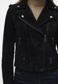 Svart mockajacka för motorcykel med diagonalt blixtlås, flera fickor med blixtlås och silverfärgade detaljer. Slät textur med en figursydd design.