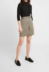 Top negro de manga larga combinado con una falda beige con lunares negros, atada en la cintura con un cinturón de tela. Unos mocasines negros completan el conjunto.