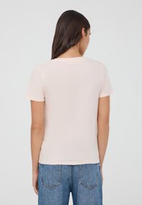 T-shirt a maniche corte di colore rosa chiaro con collo rotondo; texture morbida e design essenziale. Indossato con jeans in denim blu a vita alta.