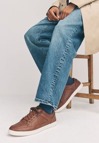 Rudi odiniai sportbačiai su baltais padais, apvalia nosimi ir raištelių užsegimu. Derinami su laisvo kirpimo mėlynais džinsais ir mėlynomis kojinėmis.