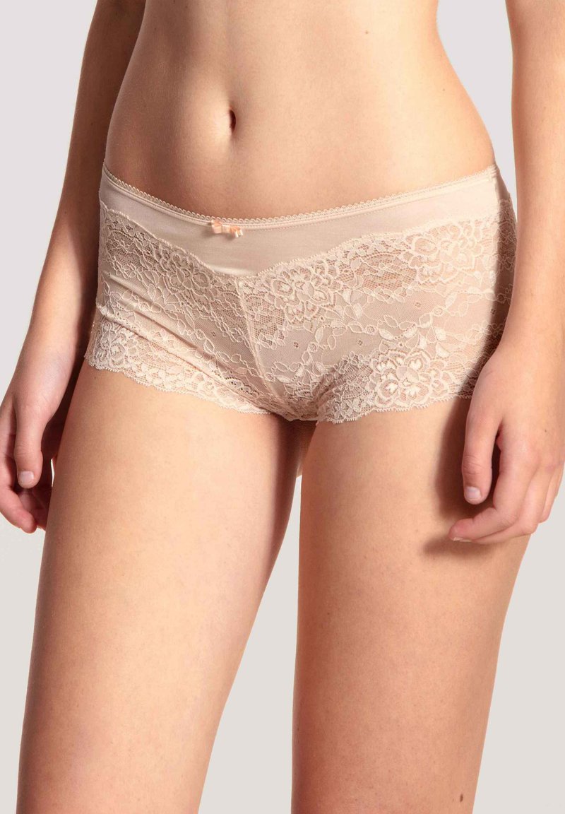 Kanten boyshorts in zacht beige met een delicate bloemenpatroon, voorzien van een gekartelde rand en een kleine strik accent op de tailleband.