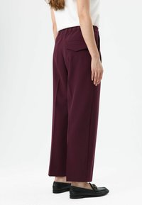 Wijdvallende broek in bordeaux met een elastische tailleband en een achterzak, gecombineerd met zwarte loafers. Glad stof met een strakke afwerking.
