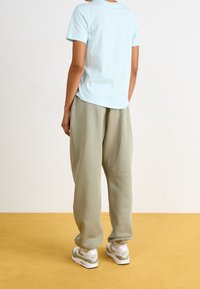 Svetle modré tričko s krátkým rukávem, volný střih, v kombinaci s volnými, světle zelenými tepláky a bílými teniskami se zelenými akcenty.