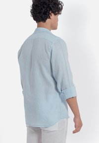 Camicia di lino blu chiaro con vestibilità su misura, colletto button-down, maniche lunghe arrotolate e orlo dritto. La vista posteriore mostra una trama sottile.