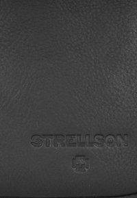 Čierna kožená peňaženka s textúrovaným povrchom; embosovaný logo "STRELLSON" s ikonou plus pod ním.