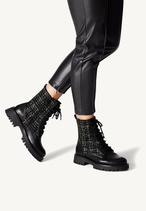 Bottes de combat noires avec une tige en tissu texturé et un design à lacets, dotées d'une semelle en caoutchouc épaisse et crantée pour une meilleure adhérence.