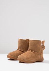 Bottines en suède marron avec doublure en peluche, bout arrondi et semelle en caoutchouc. Présente une bande cousue et une étiquette de marque à l'arrière.