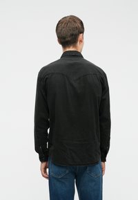 Czarna koszula z długimi rękawami, z kołnierzykiem i zaokrąglonym paskiem na plecach. Wykończona mankietami na guziki i miękką teksturą.