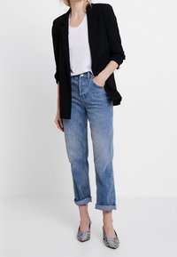 Černý upravený blazer přes bílé tričko, doplněný o světle modré zkrácené džíny a lodičky s hadím vzorem. Neformální a moderní outfit.