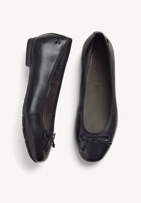 Ballerine in pelle nera con punta arrotondata, piccolo fiocco decorativo, fodera morbida e tacco basso, progettate per una vestibilità ampia.