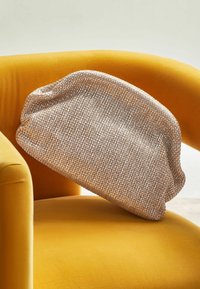 Sac argenté métallisé avec un tissage texturé, une structure souple et une forme arrondie, reposant sur une chaise rembourrée jaune.