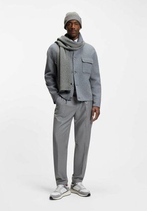Jasnoszara kurtka z mieszanki wełny z przednimi kieszeniami, szary szalik, szare plisowane spodnie i szare trampki z białymi i brązowymi akcentami.