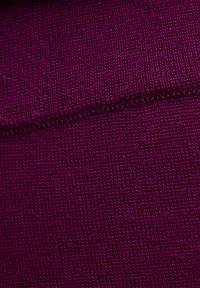 Primo piano di un tessuto viola a maglia stretta, che mostra una texture dettagliata e una cucitura visibile che corre diagonalmente.