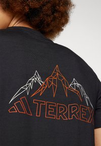 Čierne tričko s geometrickým dizajnom hory v oranžovej a bielej farbe, pod grafikou je text "TERREX". Krátke rukávy, okrúhly výstrih.