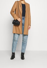 Camel wollen mix jas met een op maat gemaakt ontwerp, gedragen over een marineblauw sweater en lichtblauwe rechte jeans, gecombineerd met zwarte enkellaarsjes met hak en een zwarte clutch.