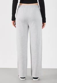 Jasnoszare dresy z luźnym krojem, elastycznym pasem i gładką fakturą, widziane z tyłu, noszone z casualowym obuwiem.