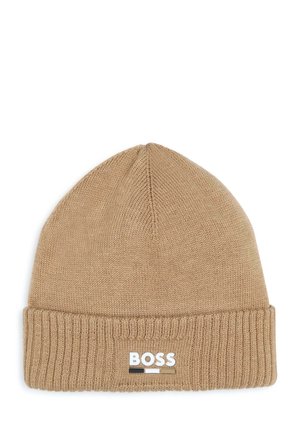Bonnet en tricot marron avec un revers. Présente un patch logo blanc avec des accents noirs et beiges. Texture douce. Design de sommet arrondi.