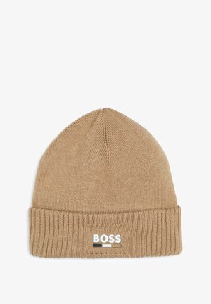 Bonnet en tricot marron avec un revers. Présente un patch logo blanc avec des accents noirs et beiges. Texture douce. Design de sommet arrondi.