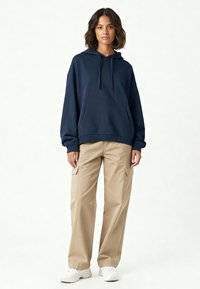 Felpa blu navy con cappuccio e lacci, tasca frontale e orlo a costine abbinata a pantaloni cargo beige chiaro con tasche laterali e vestibilità comoda.