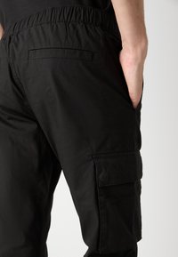 Pantaloni cargo negri din material ușor, cu talie elastică, buzunar lateral și textură netedă.