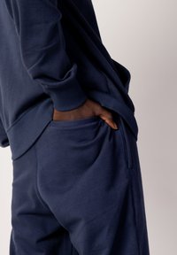Conjunto de sudadera y pantalones azul marino. Tela suave, ajuste relajado, puños acanalados y bolsillos laterales en los pantalones. Textura lisa y diseño minimalista.