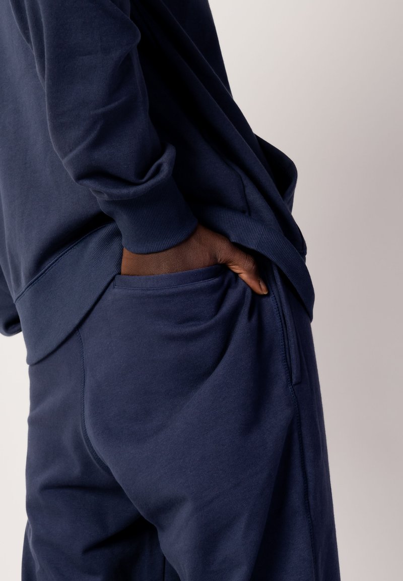 Ensemble de sweat-shirt et pantalon bleu marine. Tissu doux, coupe décontractée, poignets côtelés et poches sur les côtés du pantalon. Texture lisse et design minimaliste.