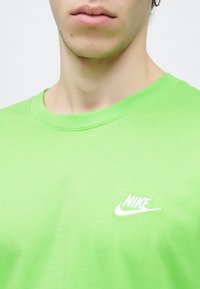 Φωτεινό πράσινο μπλουζάκι Nike με κοντά μανίκια, στρογγυλή λαιμόκοψη, λεία υφή και λευκό λογότυπο στην αριστερή πλευρά του στήθους.