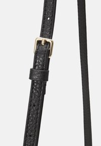 Correa de cuero negra con superficie texturizada, con una hebilla de metal dorado y una presilla de cuero. Costuras visibles y orificios de ajuste.