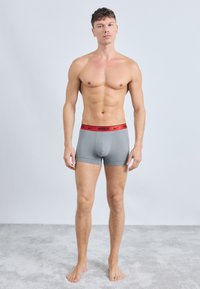 Šedé boxerky s červeným logom Nike na páske, priliehavý dizajn, jemný materiál, dĺžka do polovice stehien a hladká textúra.