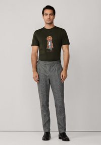 Camiseta verde de manga corta con un gráfico de perro, combinada con pantalones grises de cuadros y zapatos negros. Conjunto sencillo y casual.