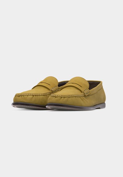 Paire de mocassins en cuir jaune moutarde avec bout arrondi et détails cousus sur fond blanc.