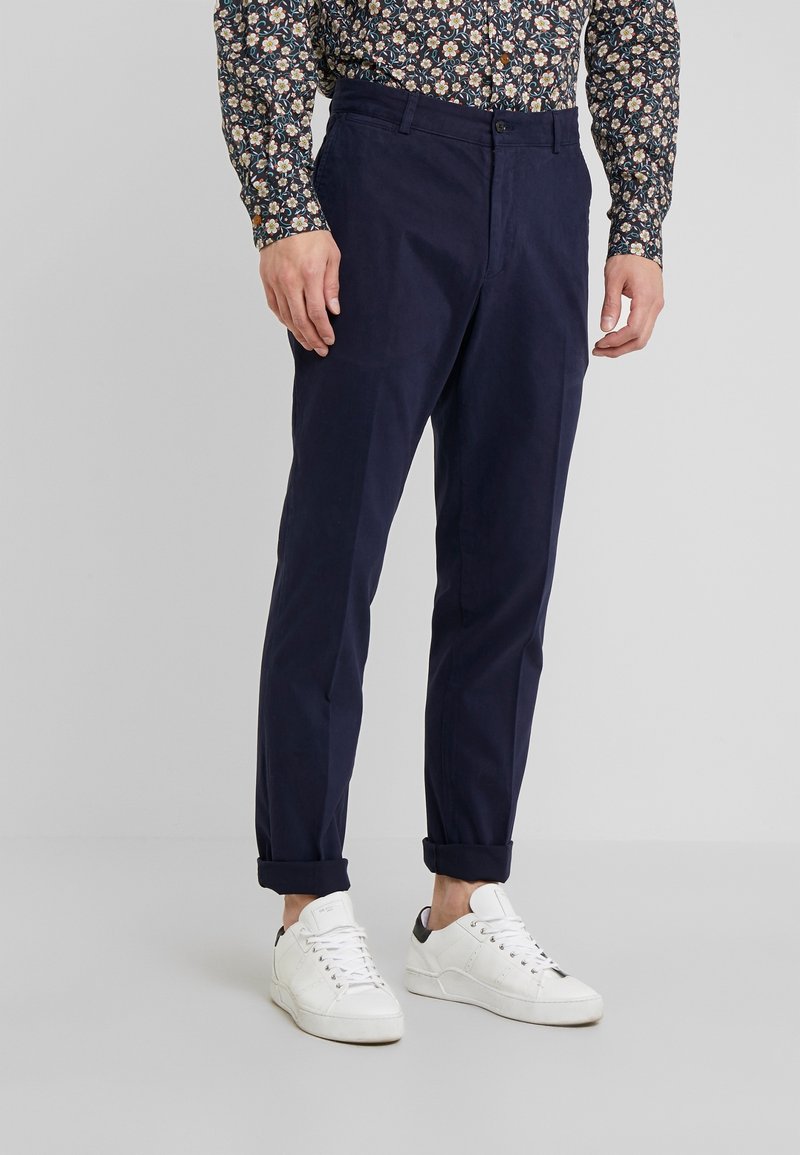 Mörkblå chinos med en avsmalnad passform, tillverkade av bomullstyg, med sidofickor, upprullade fållar och kombineras med vita sneakers.