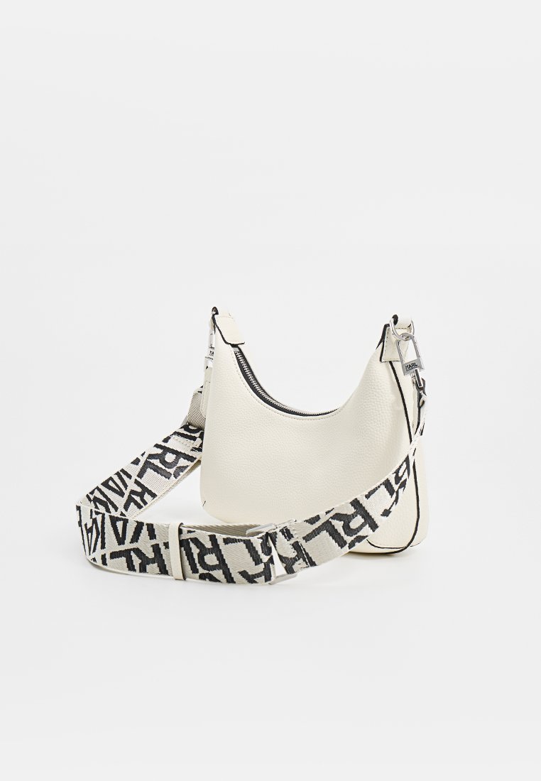 Sac à épaule en cuir blanc avec une texture et une bandoulière à logo noir et blanc contrasté. Fermeture éclair en haut.
