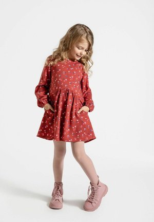 Czerwona sukienka w wzory z długimi rękawami, z marszczoną talią i kieszeniami. Połączona z różowymi trampkami i rajstopami.