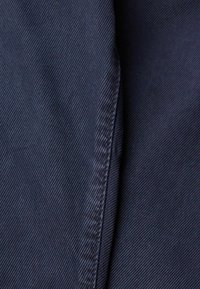 Gros plan sur un tissu bleu foncé avec une texture de tissage diagonal et des coutures visibles.