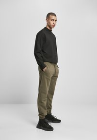 Sort langærmet skjorte, olivengrønne joggers, elastisk talje, og sorte sneakers. Enkel design, blød tekstur og afslappet pasform.