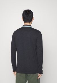 Tmavě modrá dlouhá polokošile s límečkem a modrým pruhem. Tkanina vypadá měkce, s volným střihem a minimálními designovými detaily.