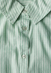 Camicia a righe verdi e bianche con colletto e chiusura con bottoni. Presenta bottoni tondi e un tessuto testurizzato.