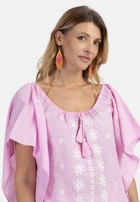 Lyserød broderet tunika med rund hals, korte frynseærmer og blomster mønstre. Har front frynse detalje og letvægts stof.