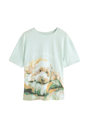 Licht muntgroen katoenen T-shirt met een illustratie van een Cockapoo die uitrust op een kussen, met kleurrijke accenten en een ontspannen ontwerp.