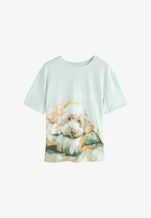Licht muntgroen katoenen T-shirt met een illustratie van een Cockapoo die uitrust op een kussen, met kleurrijke accenten en een ontspannen ontwerp.