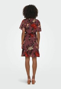 Vestido floral en malva con mangas cortas, cintura ceñida y dobladillo de volantes en capas. Presenta grandes flores rojas y crema con toques verdes.