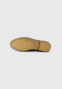 Suela de zapato con una capa exterior de goma marrón texturizada y una plantilla acolchada beige, que presenta un pequeño parche de logo en relieve.