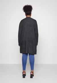 Long, dark gray knit cardigan with a relaxed fit. Features long sleeves, a slightly textured surface, and falls below the hips. Paired with blue jeans.