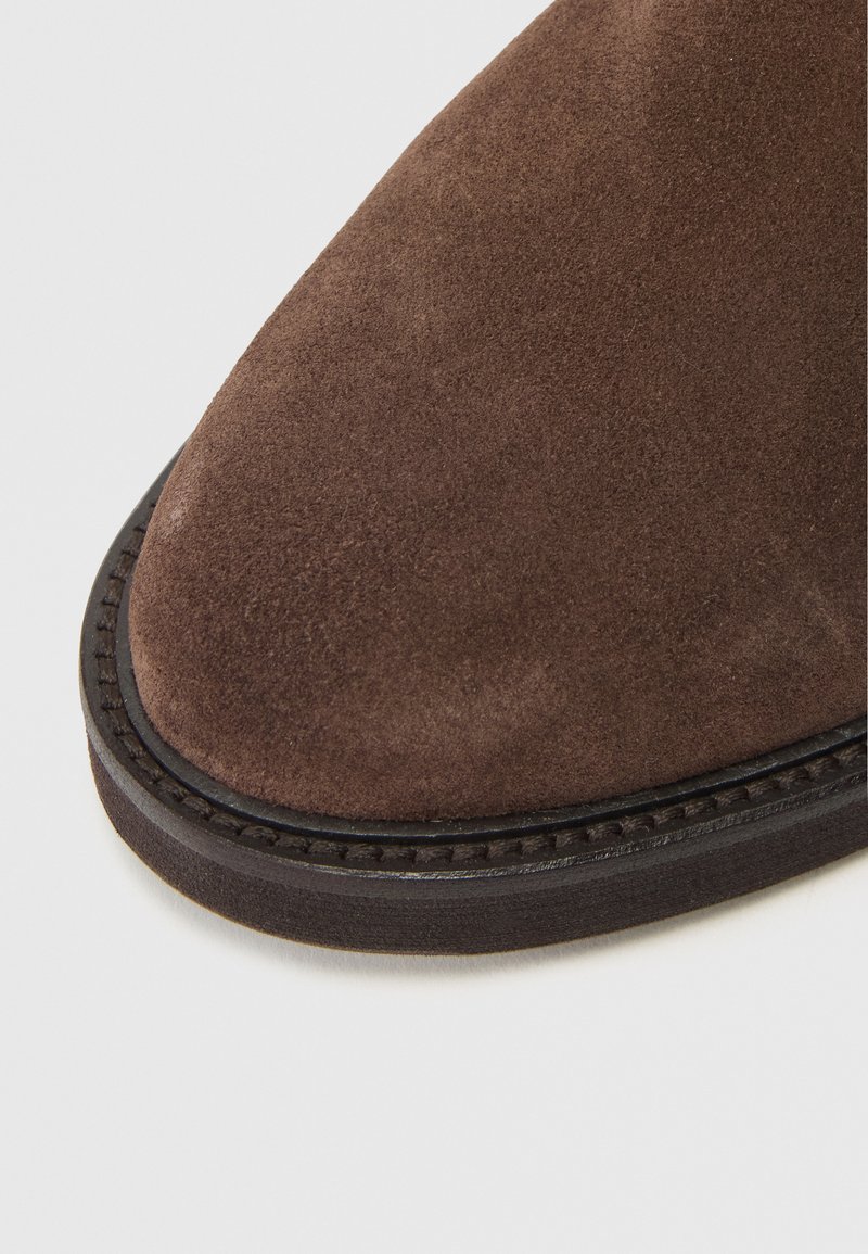 Braune Wildlederstiefel mit runder Zehenform, ausgestattet mit einer dunklen Sohle und einer Naht entlang der Kante, die eine glatte Textur betont.
