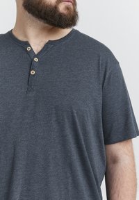 Maglietta henley a maniche corte grigia scura, realizzata in tessuto morbido, con tre bottoni in legno sul colletto e una vestibilità comoda.